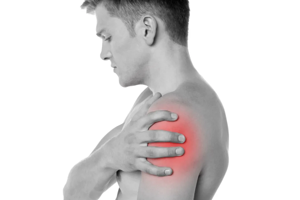 Man holding shoulder in pain, indicating shoulder strain or tear.