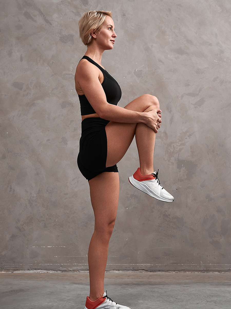 Woman in a gray room stretching her knee