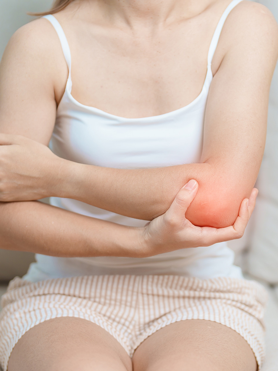 woman in a white shirt holding her elbow in pain