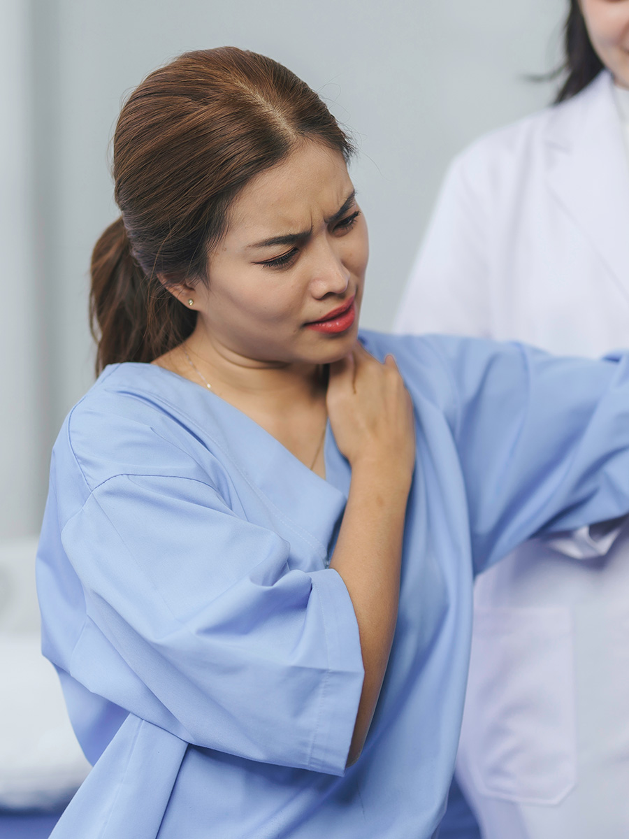 A woman in a hospital gown rubbing her shoulder