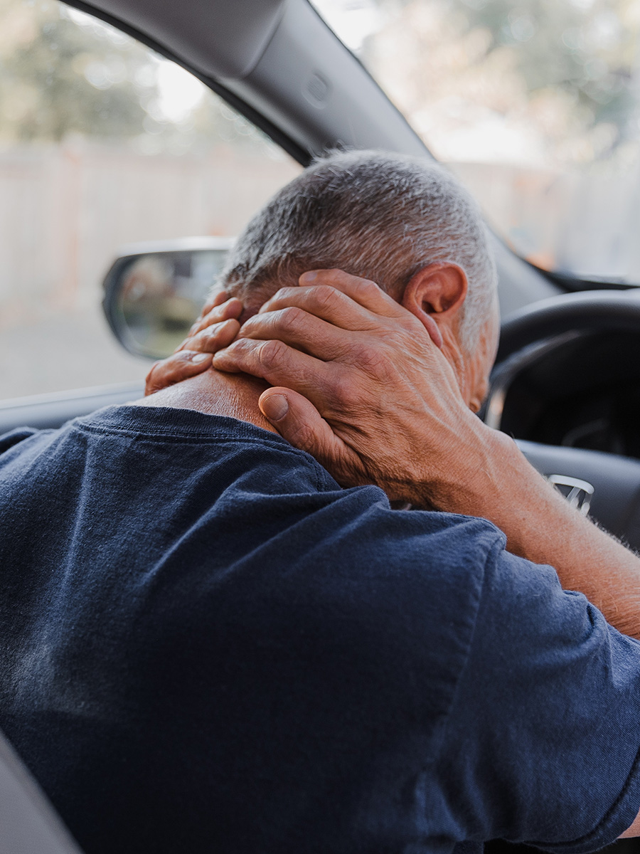 A man sitting in a car rubbing his neck